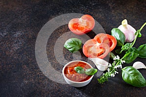 Tomato ketchup sauce in a bowl with spices, basil leaves and tomatoes on the kitchen table.