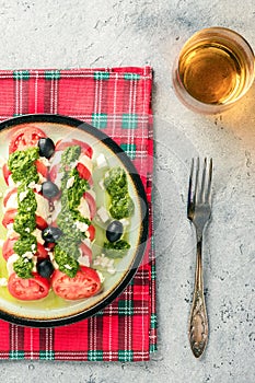 Tomato and mozzarella caprese salad and pesto sauce with olives on gray table