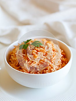 Tomato onion rice, Tamatar Biryani, jollof in white bowl on a white wooden table, vertical