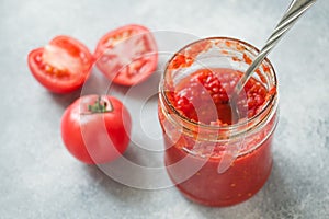 Tomato paste canned in a glass jar and fresh tomatoes on a concrete background. Fermentation of products