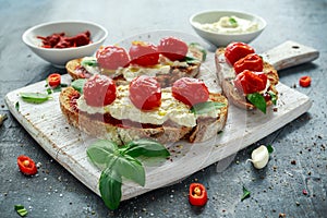 Tomato Ricotta Bruschetta with sun dried tomatoes paste, olive oil brown bread and basil in a white wooden board.