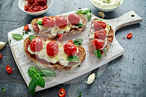 Tomato Ricotta Bruschetta with sun dried tomatoes paste, olive oil brown bread and basil in a white wooden board.