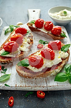 Tomato Ricotta Bruschetta with sun dried tomatoes paste, olive oil brown bread and basil in a white wooden board.