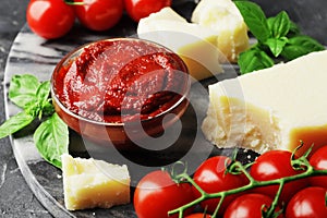 Tomato sauce in a bowl, chunks of Parmesan cheese, fresh green basil, twigs of fresh cherry