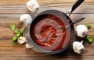 Tomato sauce in a frying pan. Basil and garlic around. View from directly above