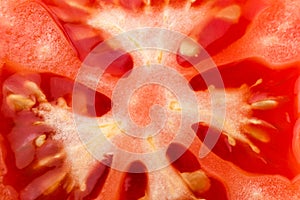 Tomato slice macro, natural background. Juicy red tomato slice closeup with flesh seeds and textures