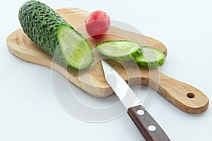Tomato, sliced cucumber and a knife on cutting board