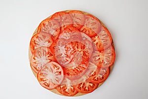 Tomato slices are laid out on a round board. White background, top view