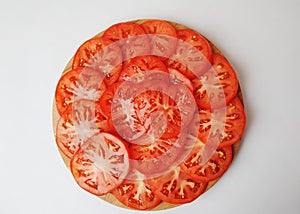 Tomato slices are laid out on a round board. White background, top view