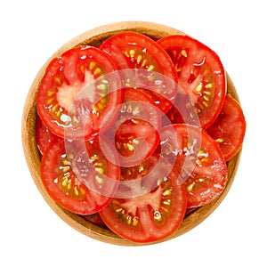Tomato slices in wooden bowl over white