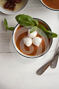Tomato soup in a bowl with mini mozzarella cheese, fresh green basil and dried tomatoes T