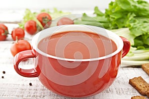 Tomato soup in red ceramic bowl on rustic wooden background. Hea