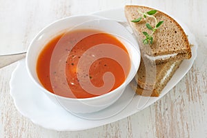 Tomato soup in white bowl with sandwich