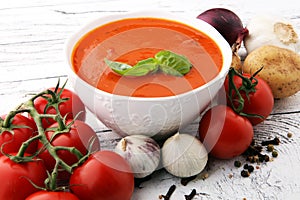 Tomato soup in a white bowl,tomatoes and parsley on a wooden bac