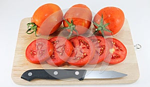 Tomato on wood chopping block with knife white background isolated