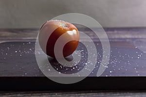 Tomato on a wood cutting board being salted for a meal