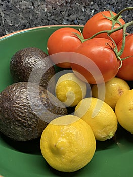 Tomatoes avocadoes and lemons in a bowl.