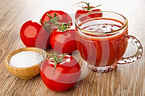 Tomatoes on branch, salt in bowl, cup of tomato juice on wooden table