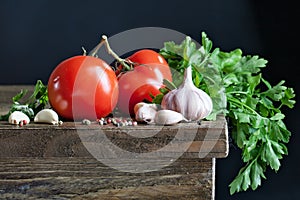 Tomatoes, garlic and herbs on the table on a dark background.