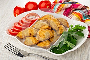Tomatoes, napkin, partitioned dish with patties, parsley, slices of tomato, fork on wooden table