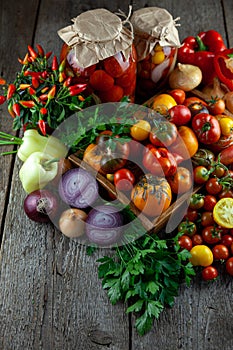 Tomatoes, peppers, onions on the table. Preservation of the autumn harvest of vegetables. Glass jar with pickled tomatoes. Wooden