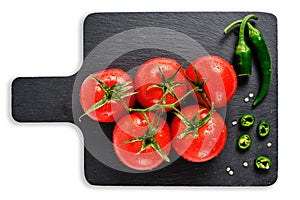 Tomatoes and pod of hot pepper on slate cutting board, isolated white background