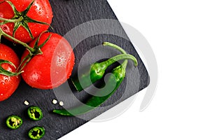 Tomatoes and pod of hot pepper on slate cutting board, isolated white background
