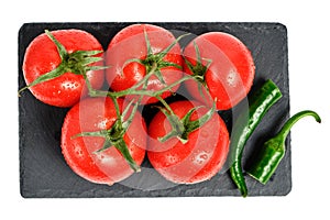 Tomatoes and pod of hot pepper on slate cutting board, isolated white background