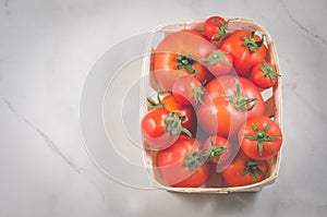 Tomatoes in a wattled container/tomatoes in a wattled container on a white marble background, top view and copyspace