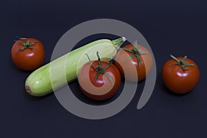 Tomatoes and zucchini on a dark background. Composition of zucchini and red tomato on a black background on a dark background.