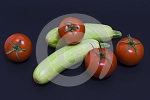 Tomatoes and zucchini on a dark background. Composition of zucchini and red tomato on a black background on a dark background.