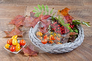 Tomatos, sprig of rowantree and autumn leaves are lying on a wooden desk. photo