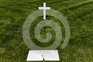 Tomb and white marble cross with flower at Arlington National Cemetery, a military cemetery in Washington DC.