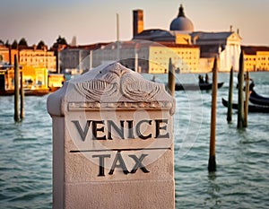 A tombstone-like marble sign with the title Venice Tax before a defocused Venetian background to illustrate the implementation of