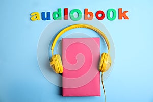 Tome with headphones and word AUDIOBOOK on blue background, flat lay
