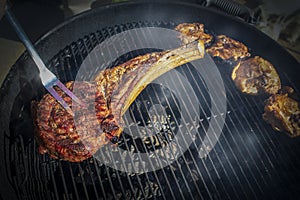 Tomohawk steak on a charcoal grill with glowing coals and smoke and a fork pressing it for doneness