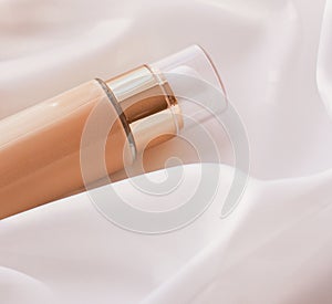 Tonal bb cream bottle make-up fluid foundation base for nude skin color on silk background, cosmetics product as luxury beauty