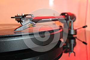 Tone arm of a modern high quality turntable record player on a vinyl analogue music LP with red backlight.