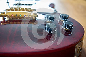 Tone And Volume Knobs On a Shiny Wine Red Guitar With Golden Hardware Placed On A Wooden Table