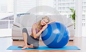 Toned blonde sitting beside exercise ball smiling at camera