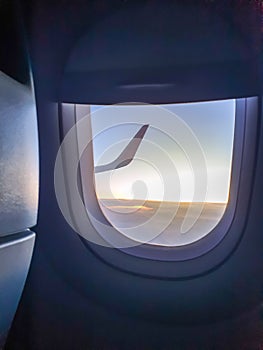 Toned image through the airplane porthole of wing in sunset light over the clouds