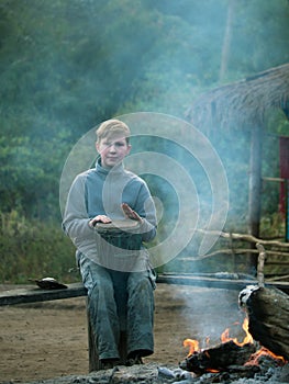 Toned image of the child sitting on the bench and playing a drum next to a burning fire