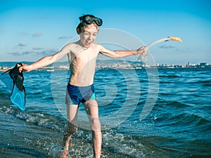 Toned image of a little boy in a mask for diving who holds in his hand flippers and snorkel and runs along the coast on the