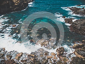 Toned image of turquoise ocean waves rolling and breaking on sharp cliffs and rocks on the shore