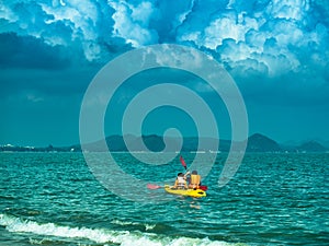 Toned image of a yellow kayak with two tourists sails on the sea on the background of dramatic sky