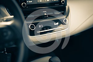 Toned photo highest temperate heat setting with knobs, digital display inside modern leather car interior, defrost mode fan at