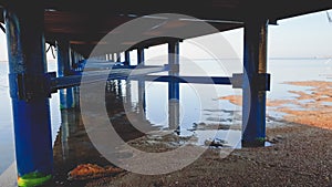 Toned photo of long row of metal columns supporting long wooden pier in the sea