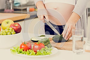 Toned photo of pregnant woman making salad on kitchen
