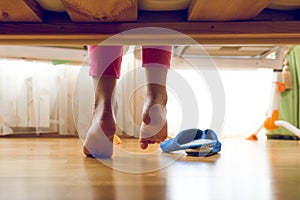Toned image from under the bed on young girl in pajamas searching for slippers