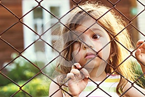 Toned portrait of Sad cute little girl looks through wire fence